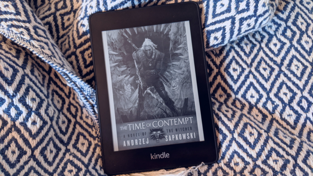 Kindle Paperwhite E-reader displaying the book cover for Time of Contempt by Andrej Sapkowski and sitting on ikat pattern blanket