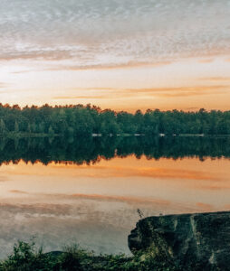 Blue and orange sunset over late with deciduous trees and reflection over the water. 