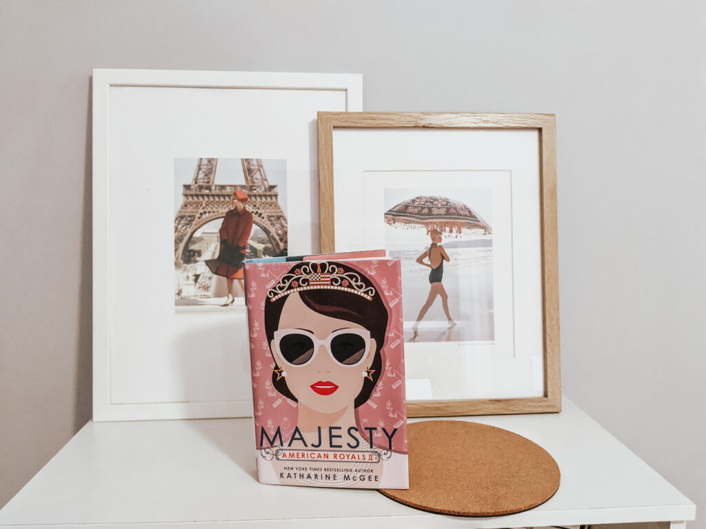 Book Majesty by Katherine McGee propped up on a bookshelf with two photos of women in frames in the background