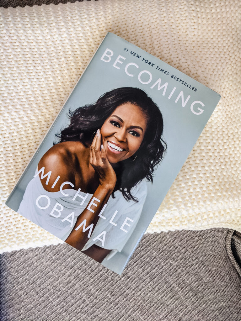 The book I read this month, Becoming by Michelle Obama, placed on a tan fabric couch and white knit blanket.