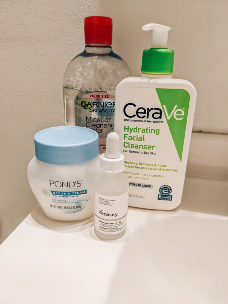 Four budget-friendly summer skincare products in my nighttime skincare routine: Clear bottle of Garnier Micellar Water, Green and white bottle of CeraVe Hydrating Facial Cleanser, short squat white and blue jar of Pond's Dry Skin Cream, and The Ordinary Hyaluronic Acid.